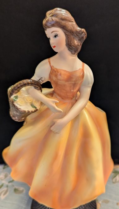 A porcelain figurine of a girl in an orange dress holding a basket.