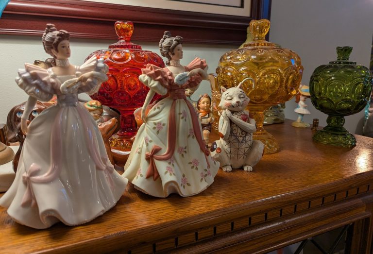 Ceramic figurines of women in elegant dresses and a small rabbit beside colorful glass vases.